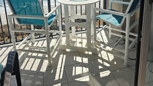 A balcony with a view of the sea, a round table with two chairs, and a small chair. - SEPT DEAL 1BR OCEANFRONT KING,pools,hotub,pristine,free parking & stunning views (Myrtle Beach)
