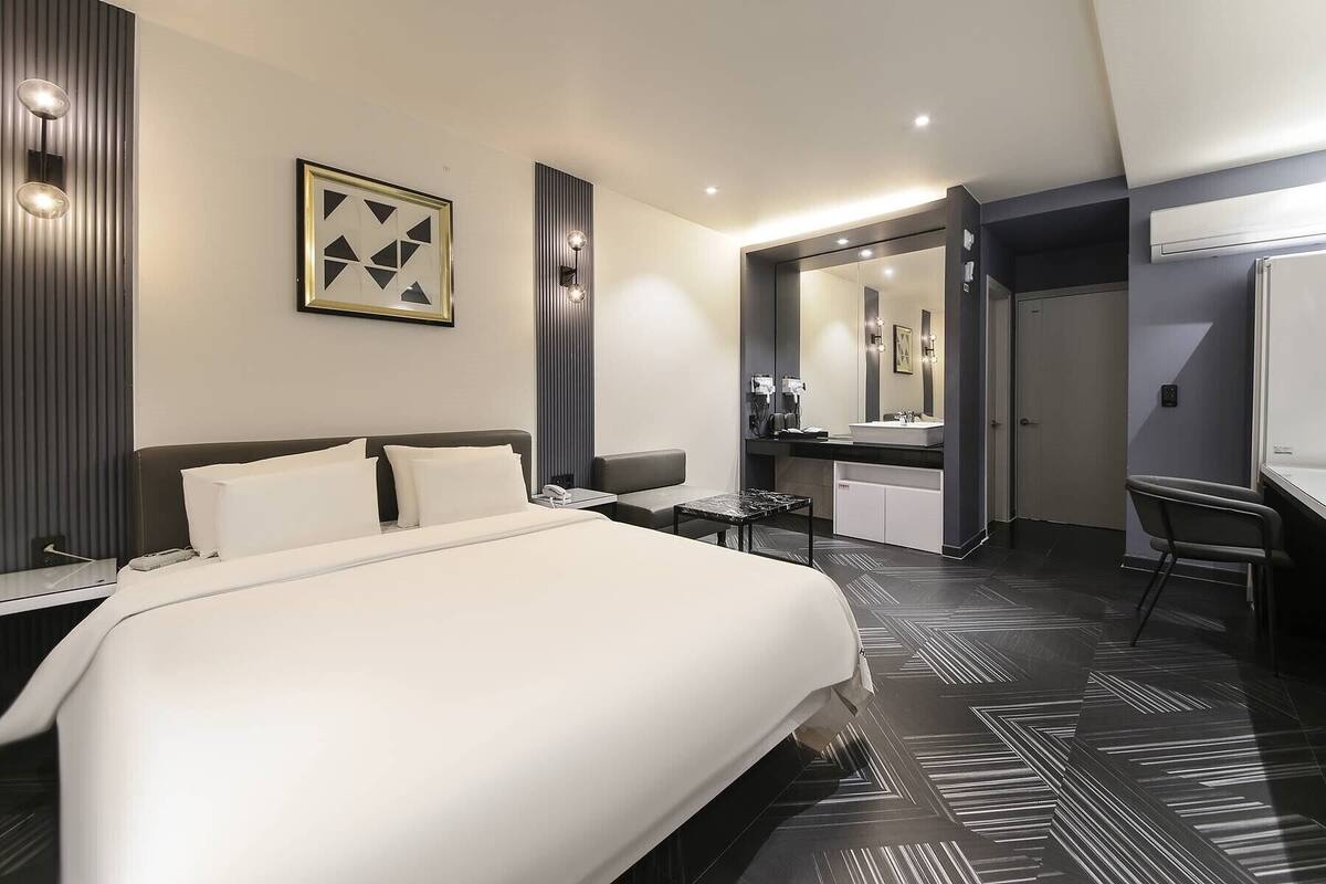 Una habitación de hotel moderna con una cama grande, un escritorio, una silla, un espejo y un baño.