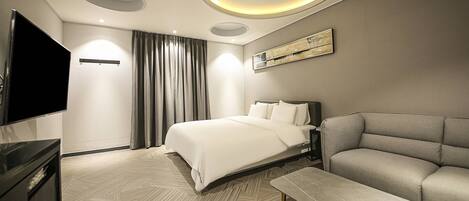 A modern hotel room with a bed, a sofa, a TV, and a painting on the wall.