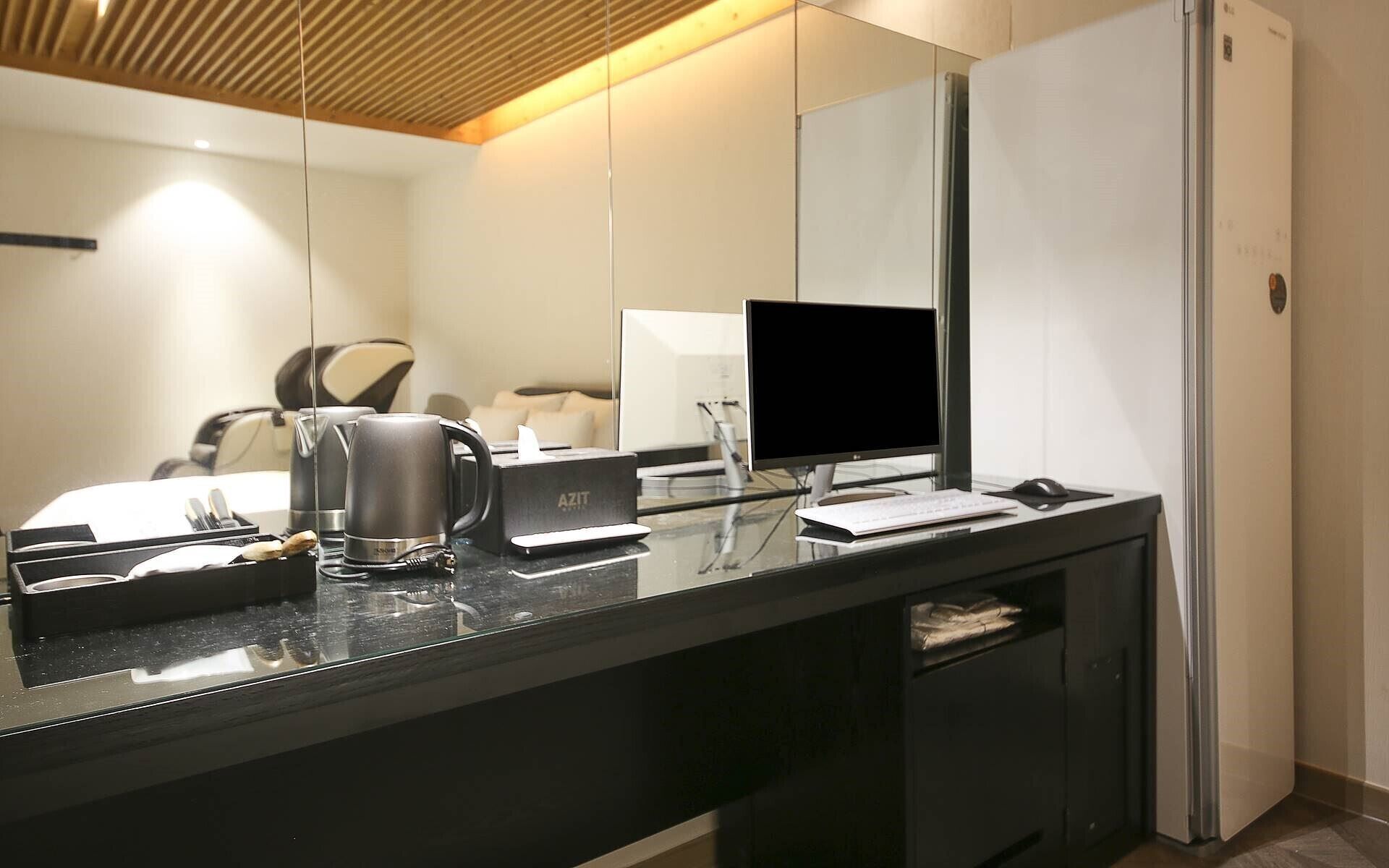 Habitación de hotel moderna con un espejo grande, un televisor de pantalla plana, una cafetera y un escritorio con teclado y ratón.