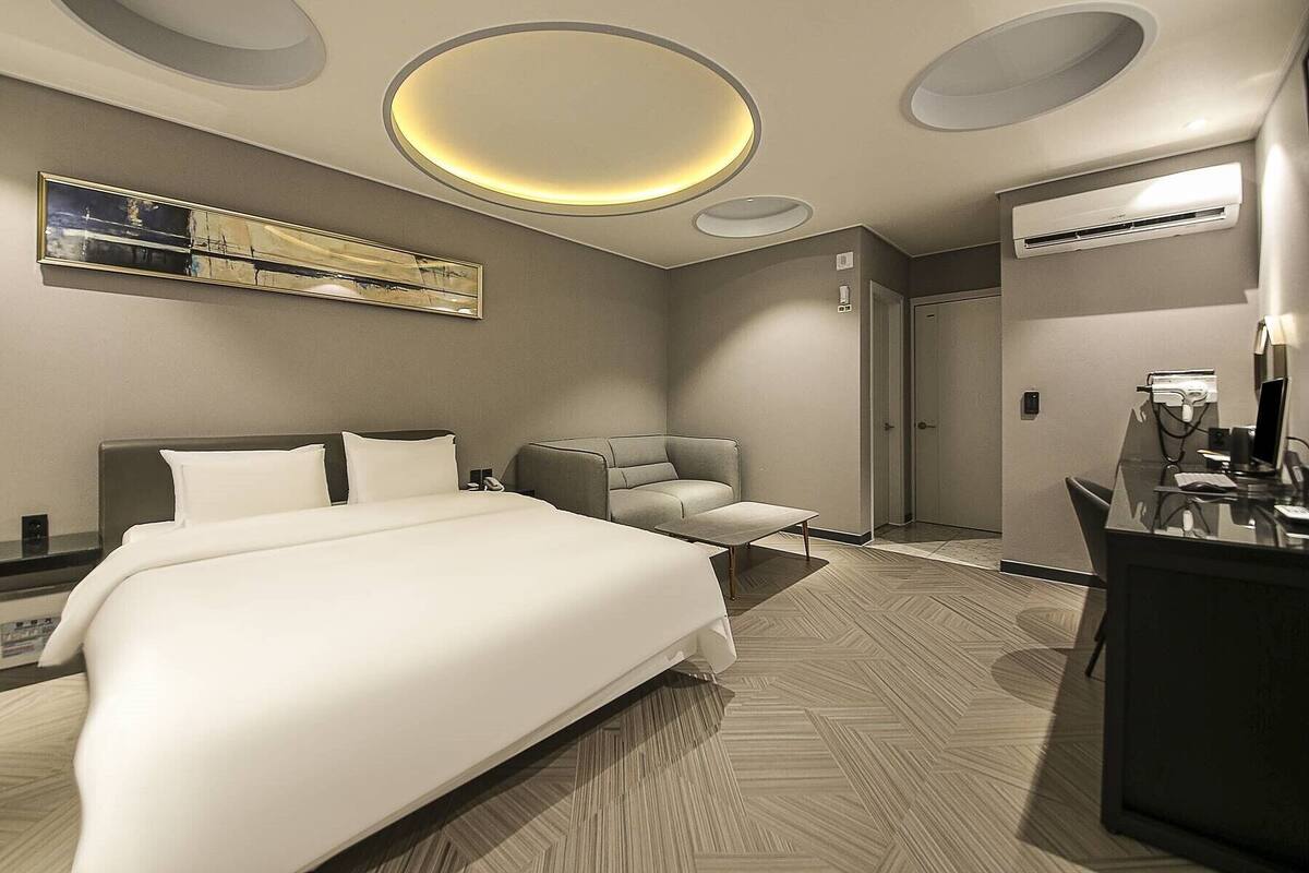 Habitación de hotel moderna con una cama grande, una zona de estar, un escritorio con computadora y un espejo.