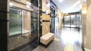 A modern lobby with a bench, glass doors, and a tiled floor. - Hotel Azit - Sinsigaji (Jeonju)