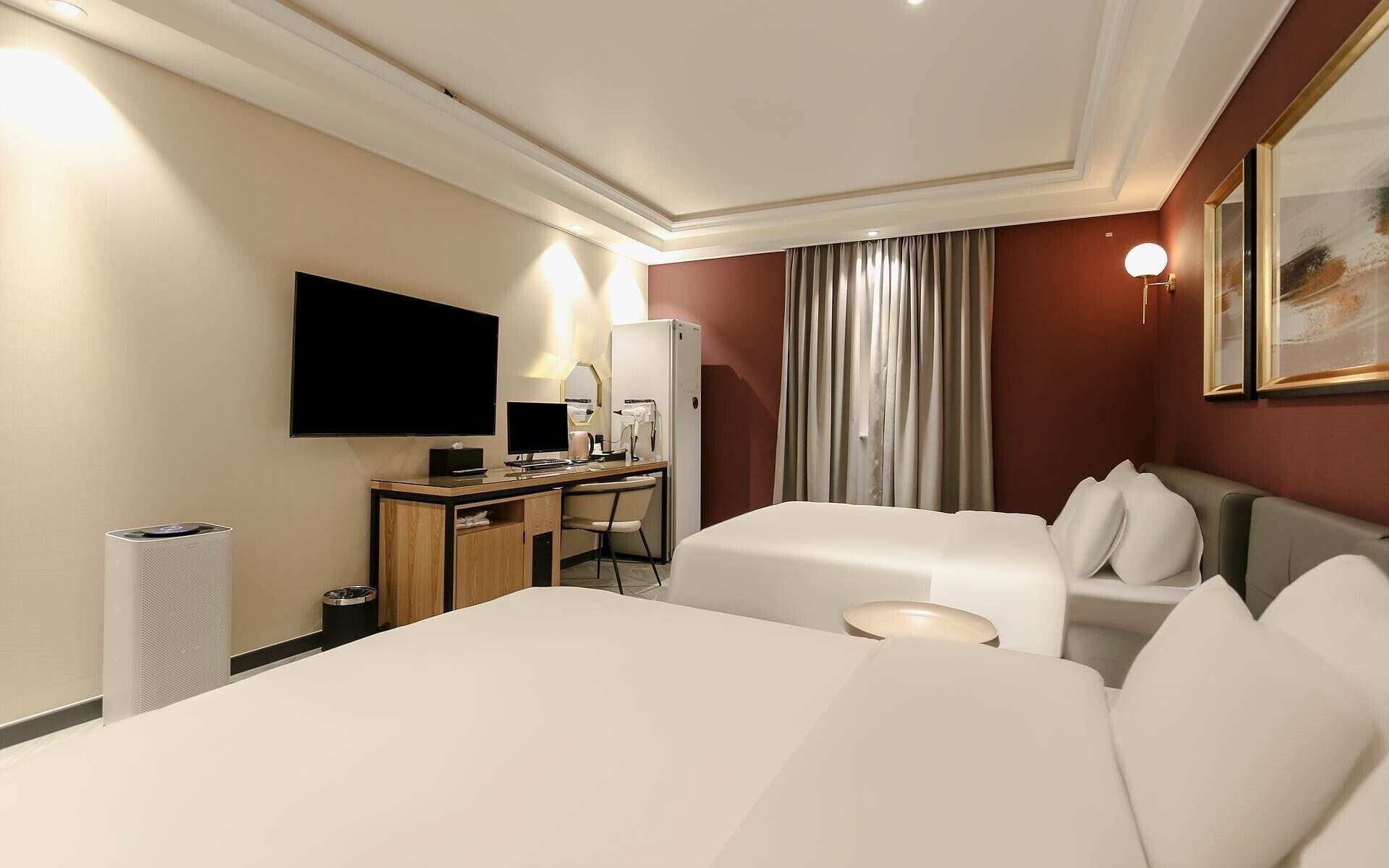 Habitación de hotel con cama, escritorio, computadora, televisor y minibar.
