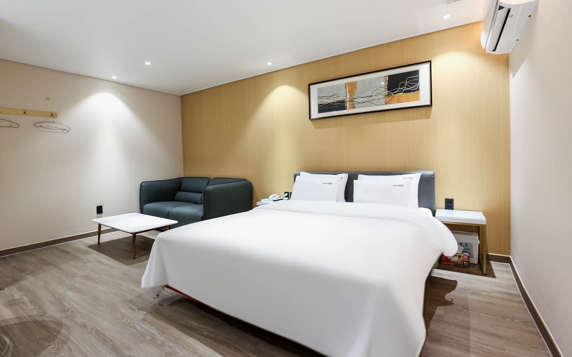 Moderni hotellihuone, jossa on suuri sänky, oleskelualue sohvineen ja pieni pöytä sekä seinälle asennettu ilmastointilaite.