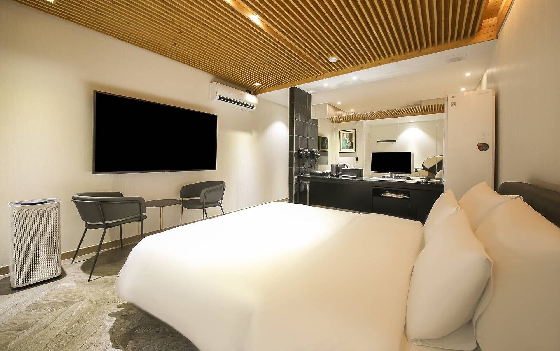 Een moderne hotelkamer met een groot bed, een flatscreen televisie, een bureau met een computer, een spiegel en een zitje.