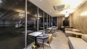 A modern indoor space with a glass wall, a car in the background, and a seating area with tables and chairs. - Hotel Azit - Sinsigaji (Jeonju)