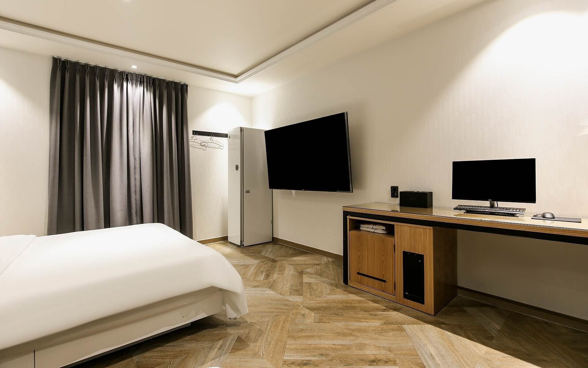 Habitación de hotel con cama, escritorio con ordenador, televisor de pantalla plana y armario.