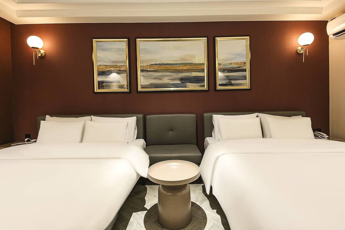 Una habitación de hotel con dos camas, una mesita redonda y tres cuadros enmarcados en la pared.