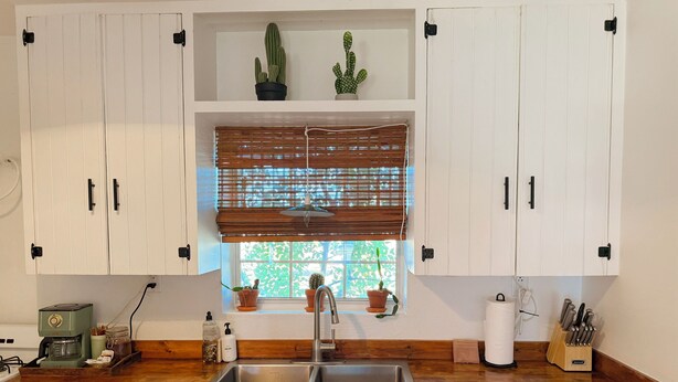 A kitchen with white cabinets, a wooden countertop, a stainless steel sink, and a window with blinds. - Casa de Conejito: Comfy Marfa Retreat (Marfa)