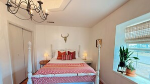 A bedroom with a bed, two bedside tables, a chandelier, a bull's head decoration, a window with plants, and a door. - Casa de Conejito: Comfy Marfa Retreat (Marfa)