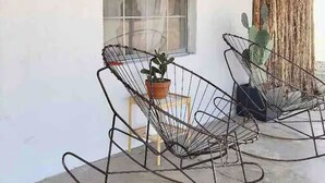 Two metal rocking chairs with potted plants, positioned outside a building with a window and a wooden door. - Casa de Conejito: Comfy Marfa Retreat (Marfa)