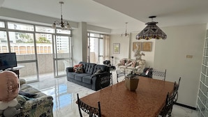 Uma sala de estar ampla com uma mesa de jantar, sofás e uma janela grande com vista para o exterior.