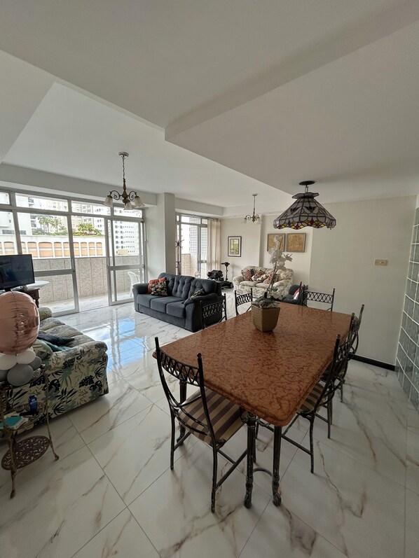A spacious living area with a dining table, sofas, and a large window offering a view of the outside.
