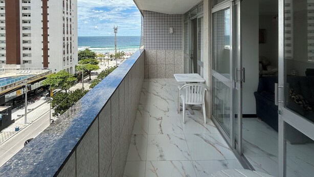 Uma varanda com vista para a praia e edifícios altos, uma mesa pequena e uma cadeira.