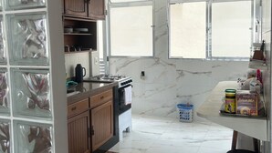 Uma cozinha com fogão a gás, armários de madeira, revestimento de mármore e uma janela com persianas.