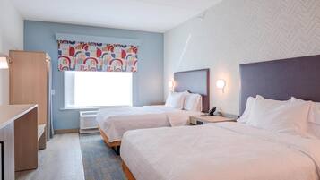 Habitación de hotel con dos camas, un escritorio y una ventana con cortina colorida.