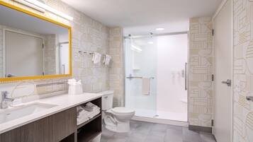 Une salle de bain moderne avec un grand miroir, des éléments d’ameublement blancs et un papier peint à motifs.