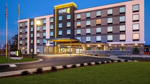 A modern hotel with a prominent "HOME 2" sign, a well-lit entrance, and a landscaped driveway. - Home2 Suites By Hilton Smithfield Selma (Smithfield)