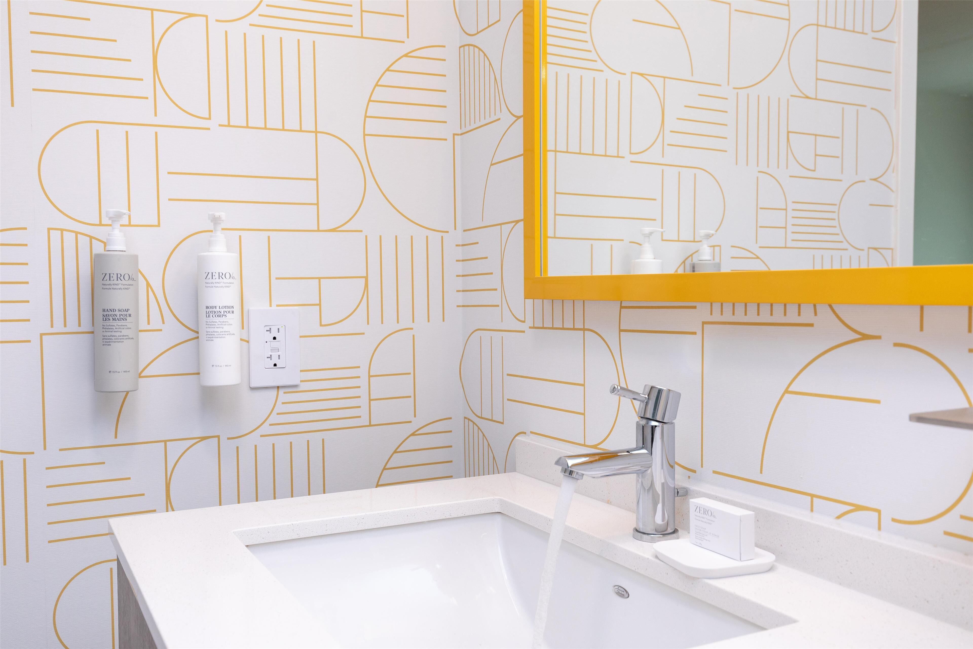 A modern bathroom with a geometric patterned wall, a white sink, and a mirror with a yellow frame.