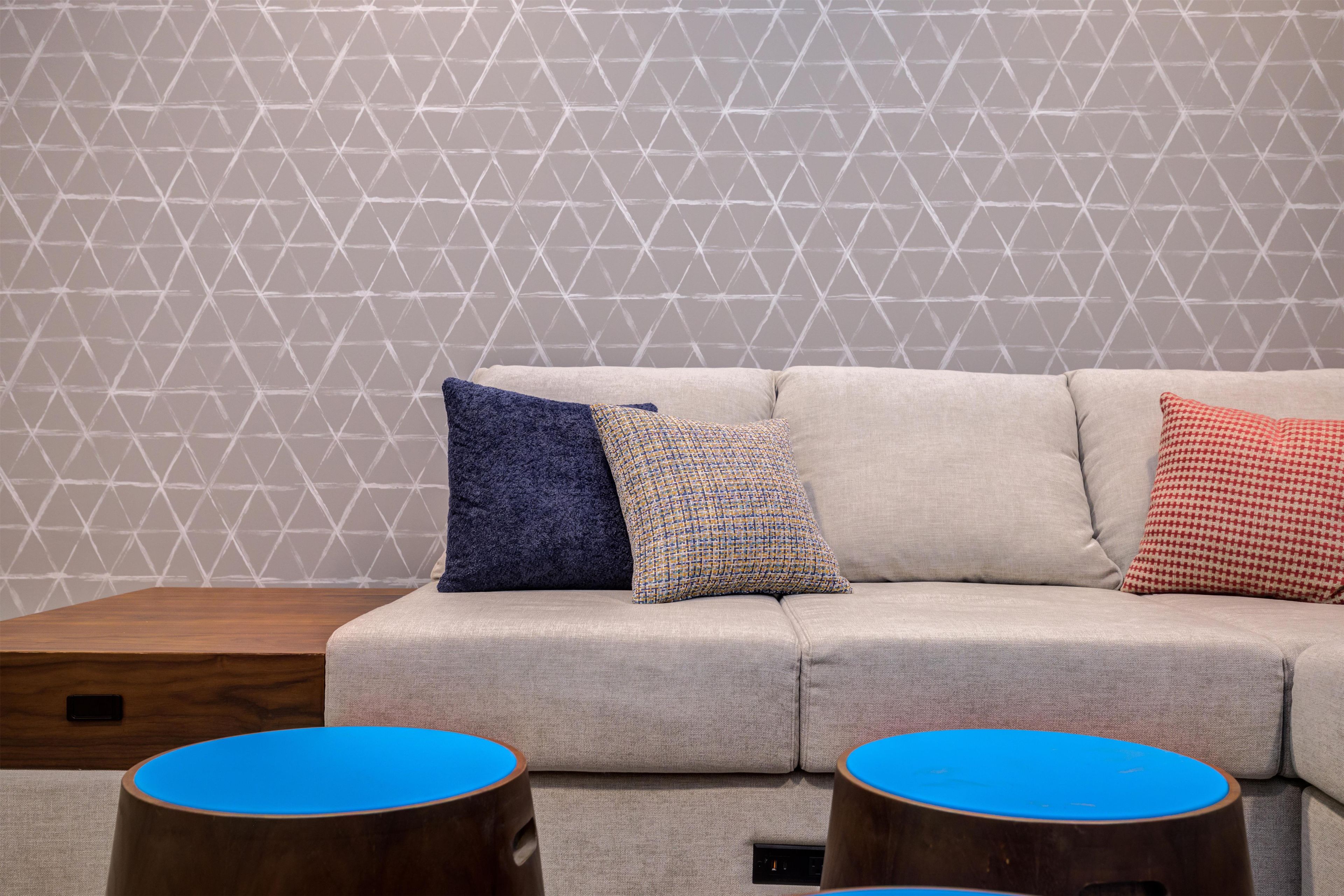 A modern living room with a geometric-patterned wall, a grey sofa, and two round wooden side tables with blue tops.