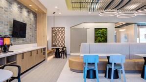 A modern kitchen with a built-in TV, wooden cabinets, and a white countertop. - Home2 Suites By Hilton Smithfield Selma (Smithfield)