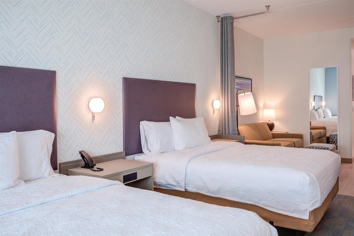 A hotel room with two beds, a desk, a chair, and a mirror.