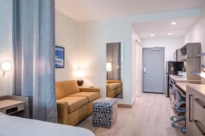 Et hotelværelse med sofa, skærm og et sengebord, lampe og et spejl.