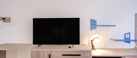 Una habitación moderna con una televisión de pantalla plana montada en un mueble de madera, un escritorio con una lámpara y una silla.