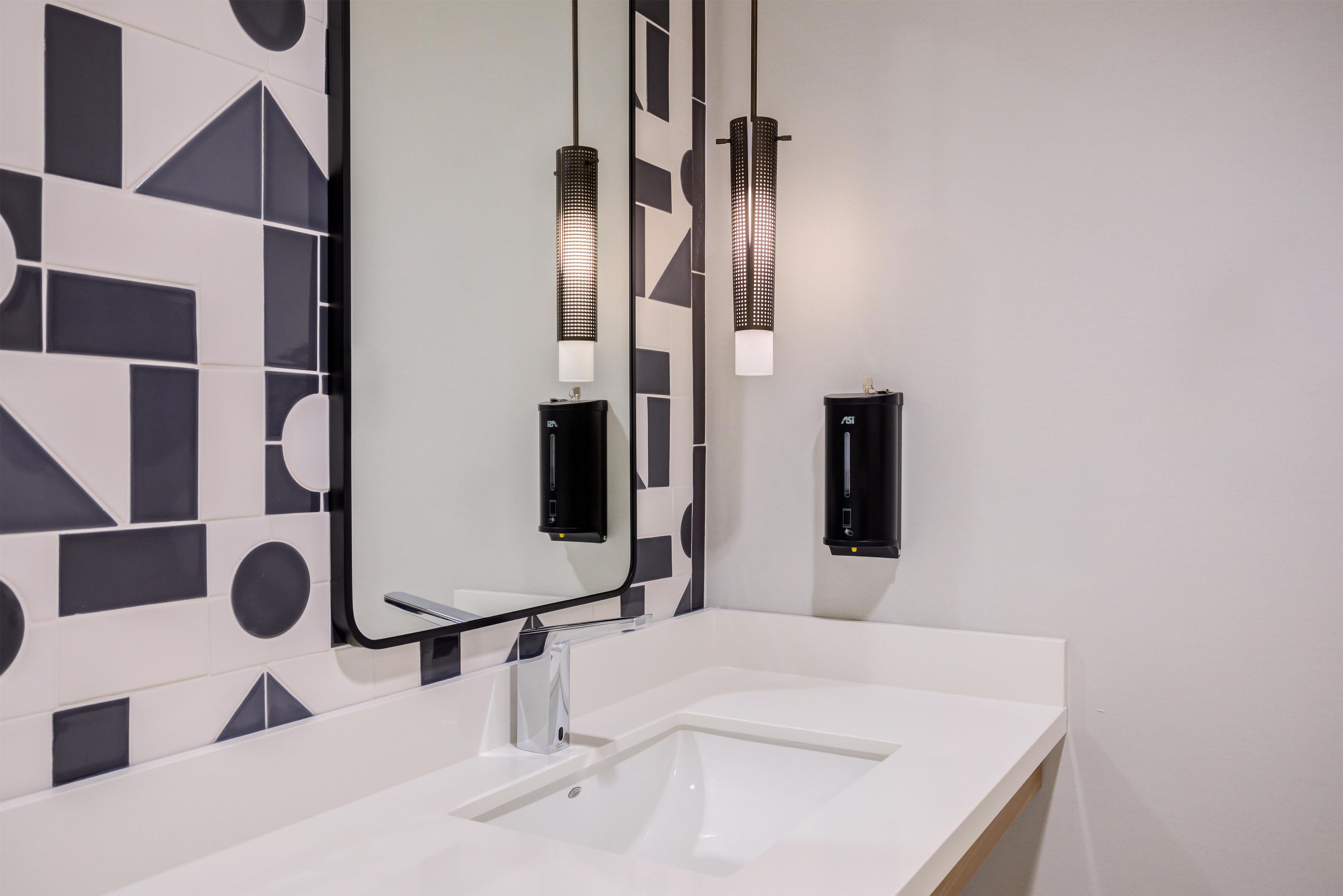 A modern bathroom with a white sink, a large mirror, and two wall-mounted lights.