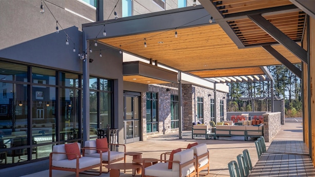 An outdoor seating area with modern furniture and a wooden pergola. - Home2 Suites By Hilton Smithfield Selma (Smithfield)