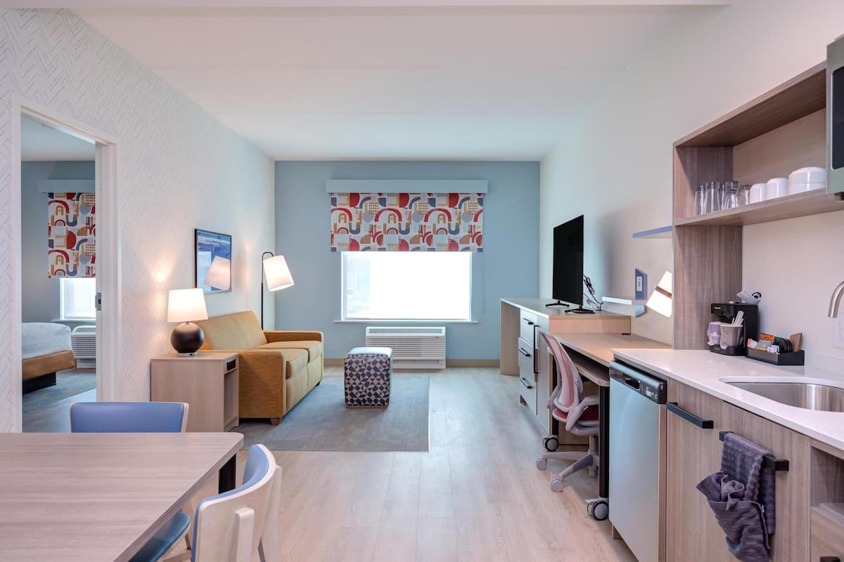 A modern hotel room with a kitchenette, a dining area, a bed, and a bathroom.
