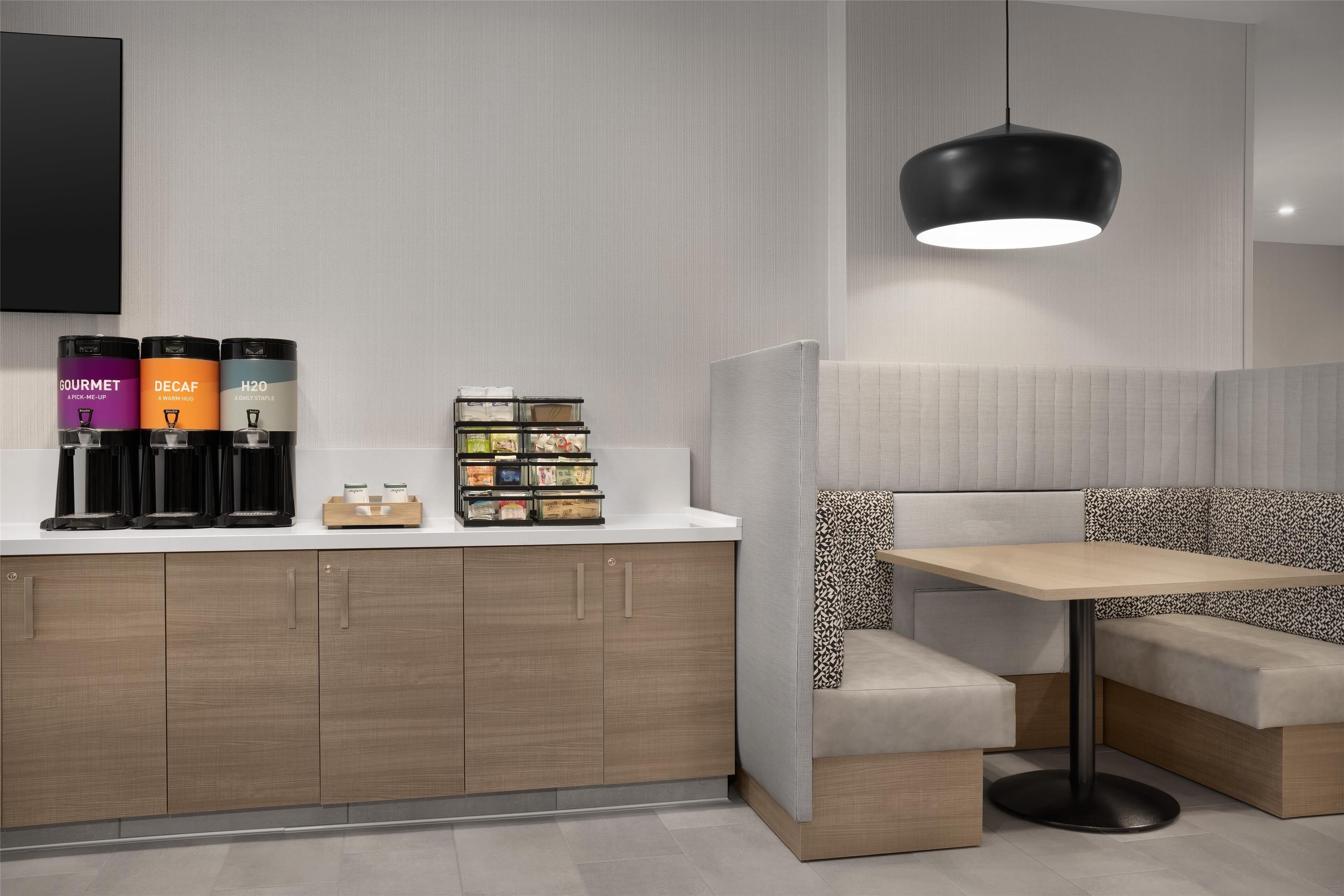 A modern kitchen with wooden cabinets, a coffee station, and a seating area with a table and bench.