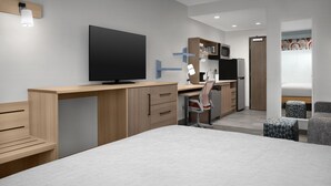 Un dormitorio moderno con una cama grande, un escritorio con computadora, un televisor y un microondas.