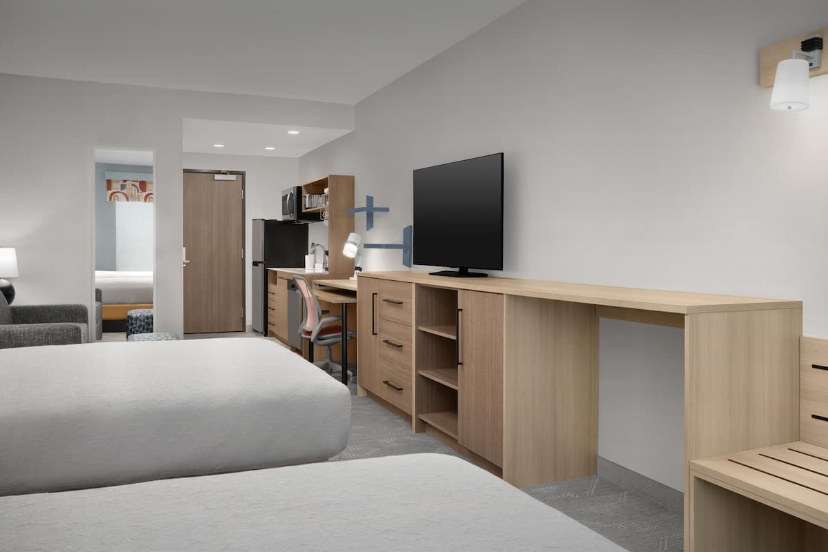 A modern hotel room with a large bed, a desk with a flat-screen TV, a chair, and a wardrobe.