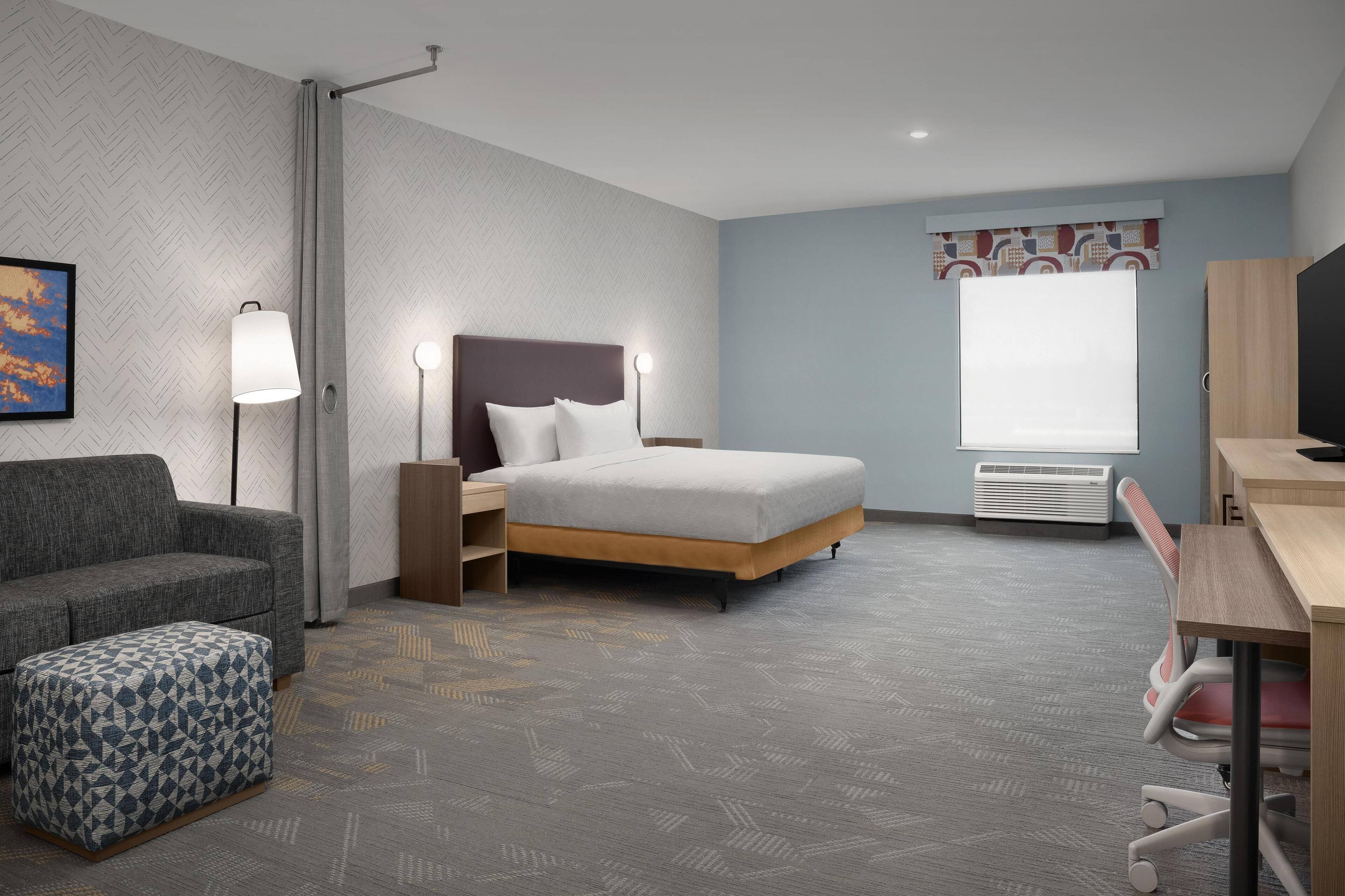 Ein Hotelzimmer mit Bett, Schreibtisch, Sessel, Sofa und Pouf mit Muster.