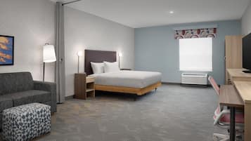 Ein Hotelzimmer mit Bett, Schreibtisch, Sessel, Sofa und Pouf mit Muster.