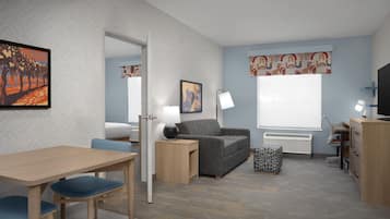 A modern hotel room with a herringbone-patterned wall, a grey sofa, a wooden desk, a television, and a large window with patterned curtains.