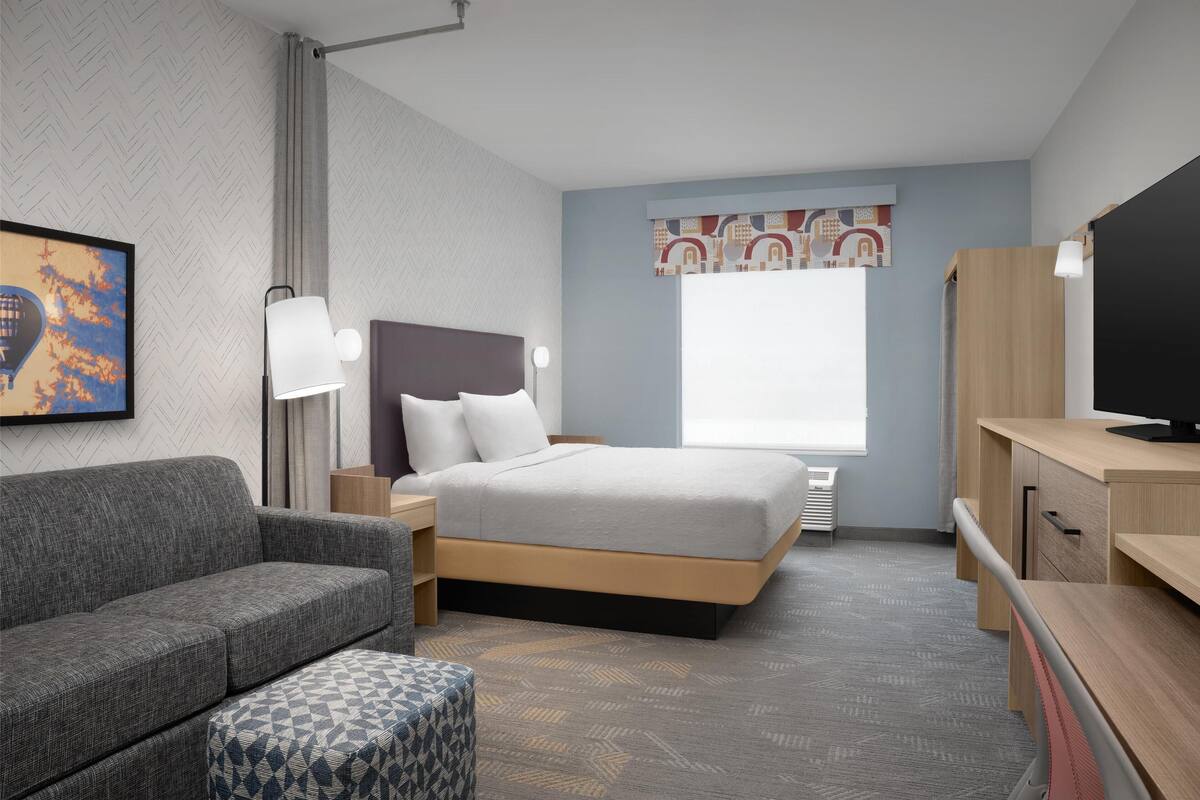 A modern hotel room with a bed, a sofa, a desk, and a TV.