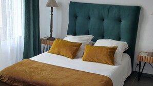 Una cama bien hecha con un cabecero tapizado en verde, almohadas blancas y mostaza, y una colcha marrón a rayas.