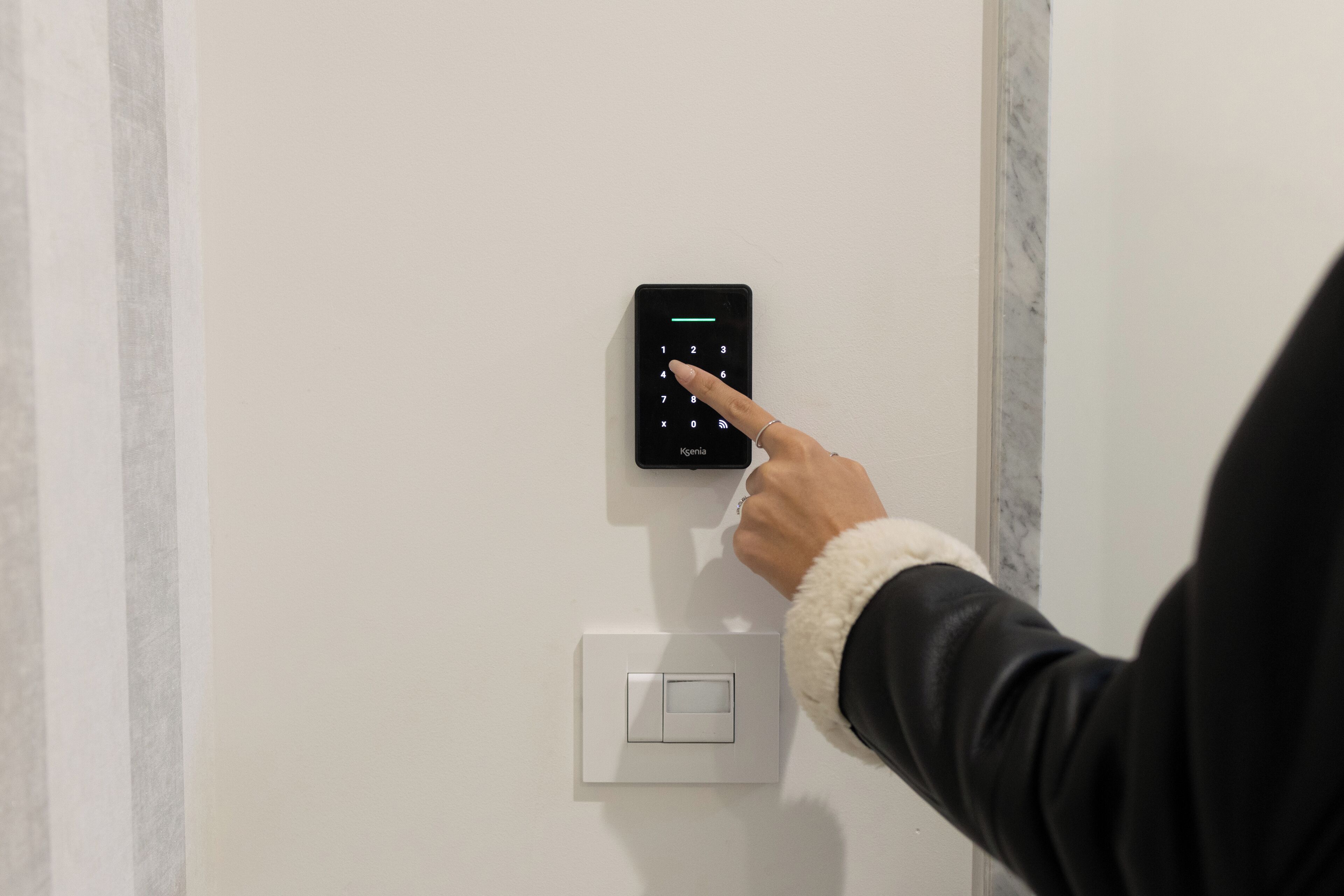 Una persona utilizando un teclado electrónico en una pared blanca, con un interruptor de luz estándar debajo.