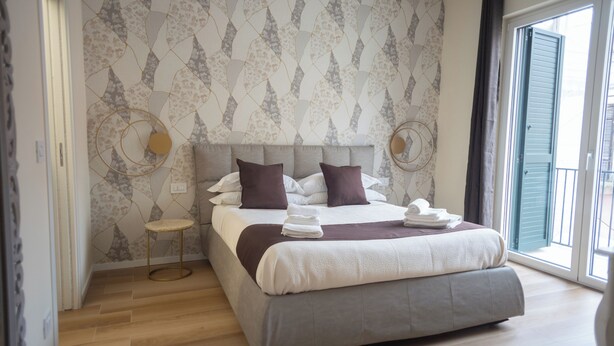 A modern bedroom with a large bed, a small side table, and a view of the outside through a sliding door. - Dimora Amelia Apartment 2, spacious apartment tastefully finished. (Bitonto)