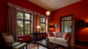 A cozy room with a sofa, armchair, and coffee table. There are large windows with curtains, a lamp, and a vase on the table. - Bluechip Leisure Summerhill Bungalow (Nuwara Eliya)