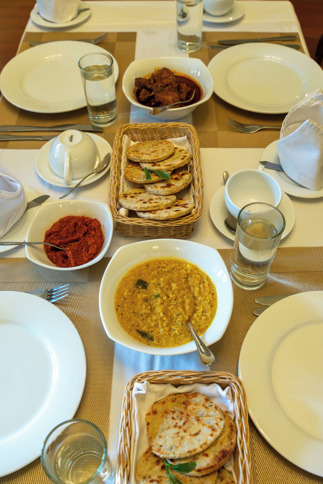Een gedekte tafel met borden, kommen, glazen en een mand met platbrood.