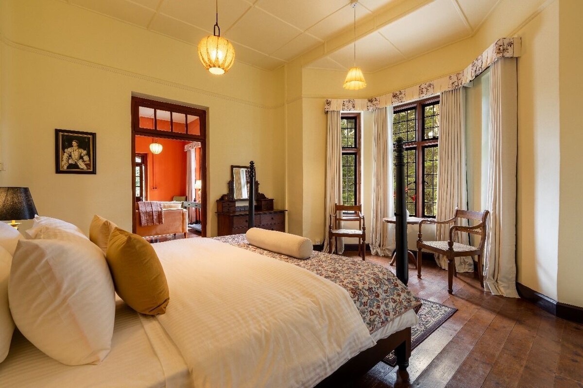 A hotel room with a large bed, two chairs, a desk, and a window with curtains.