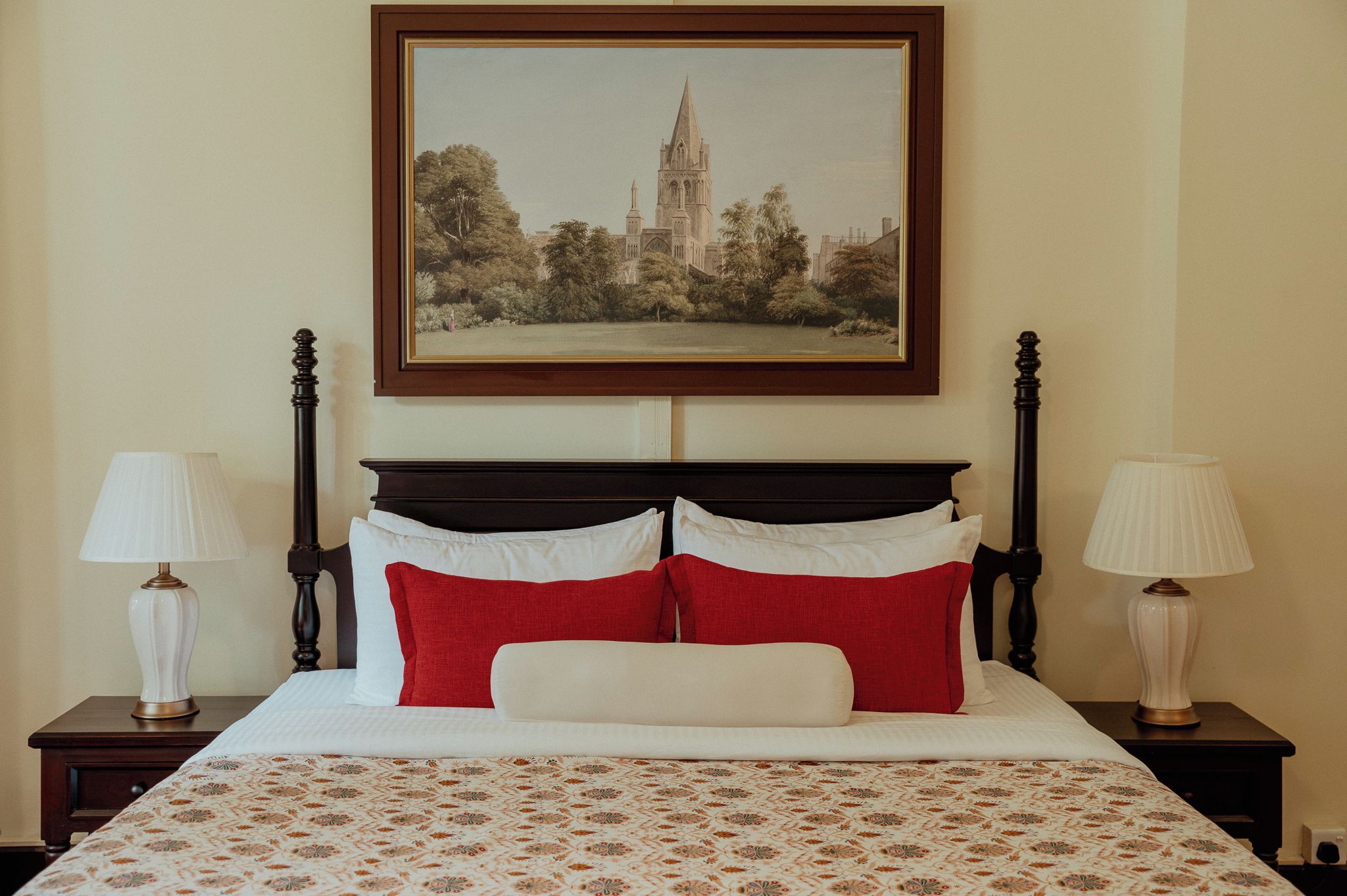 Una cama con un edredón estampado, dos mesitas de noche con lámparas y un cuadro enmarcado sobre la cama.
