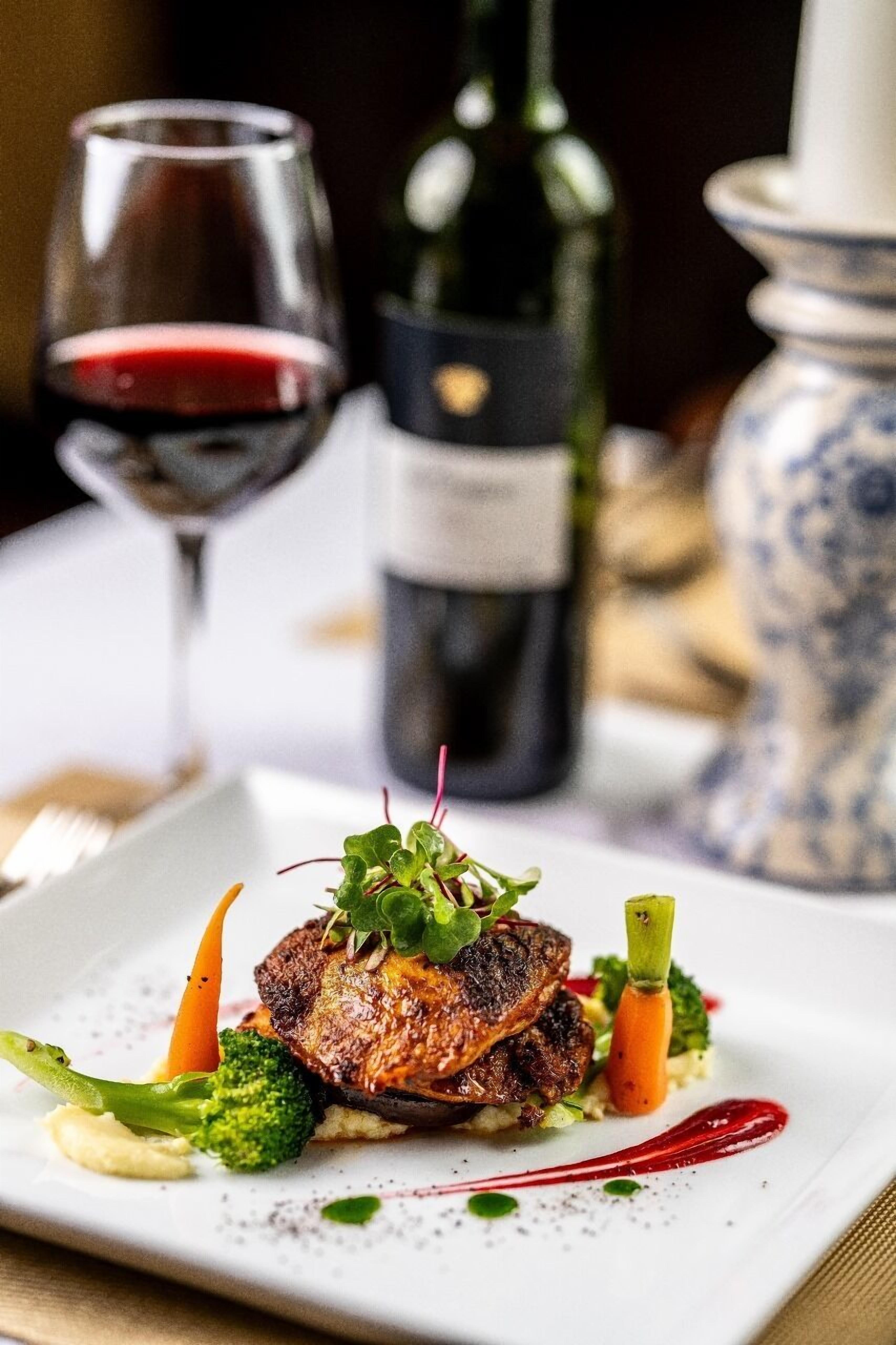 A plate of food with a glass of red wine and a bottle of wine in the background.
