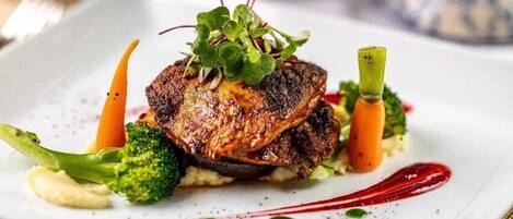 A plate of food with a glass of red wine and a bottle of wine in the background.