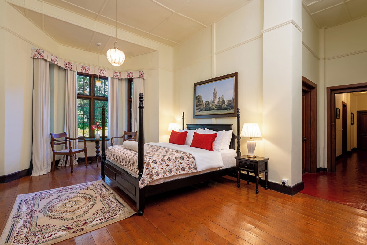 A four-poster bed with red and white bedding, a nightstand with a lamp, and a large window with curtains.
