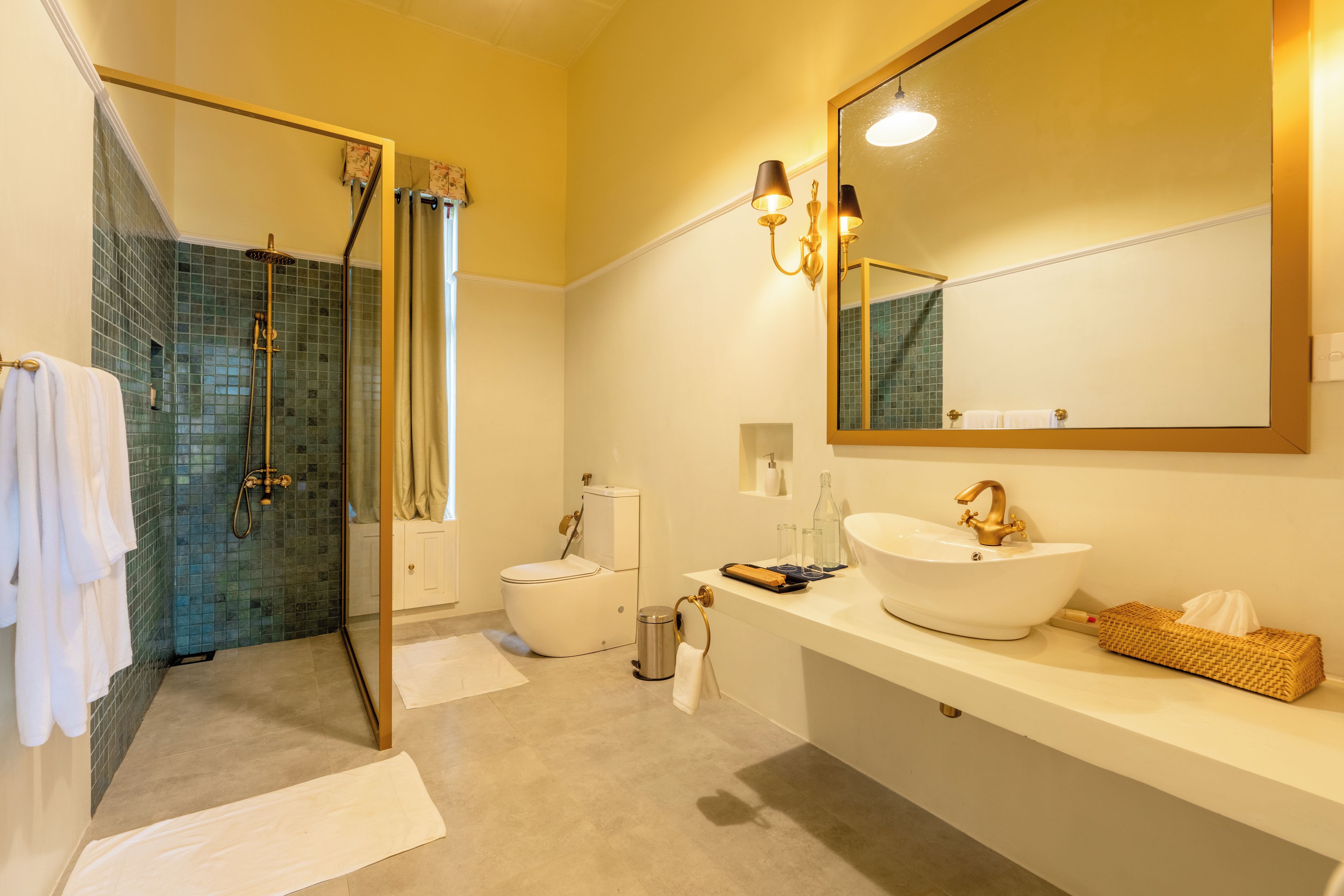 A modern bathroom with a glass shower enclosure, a white toilet, a large mirror, and a white sink with gold fixtures.