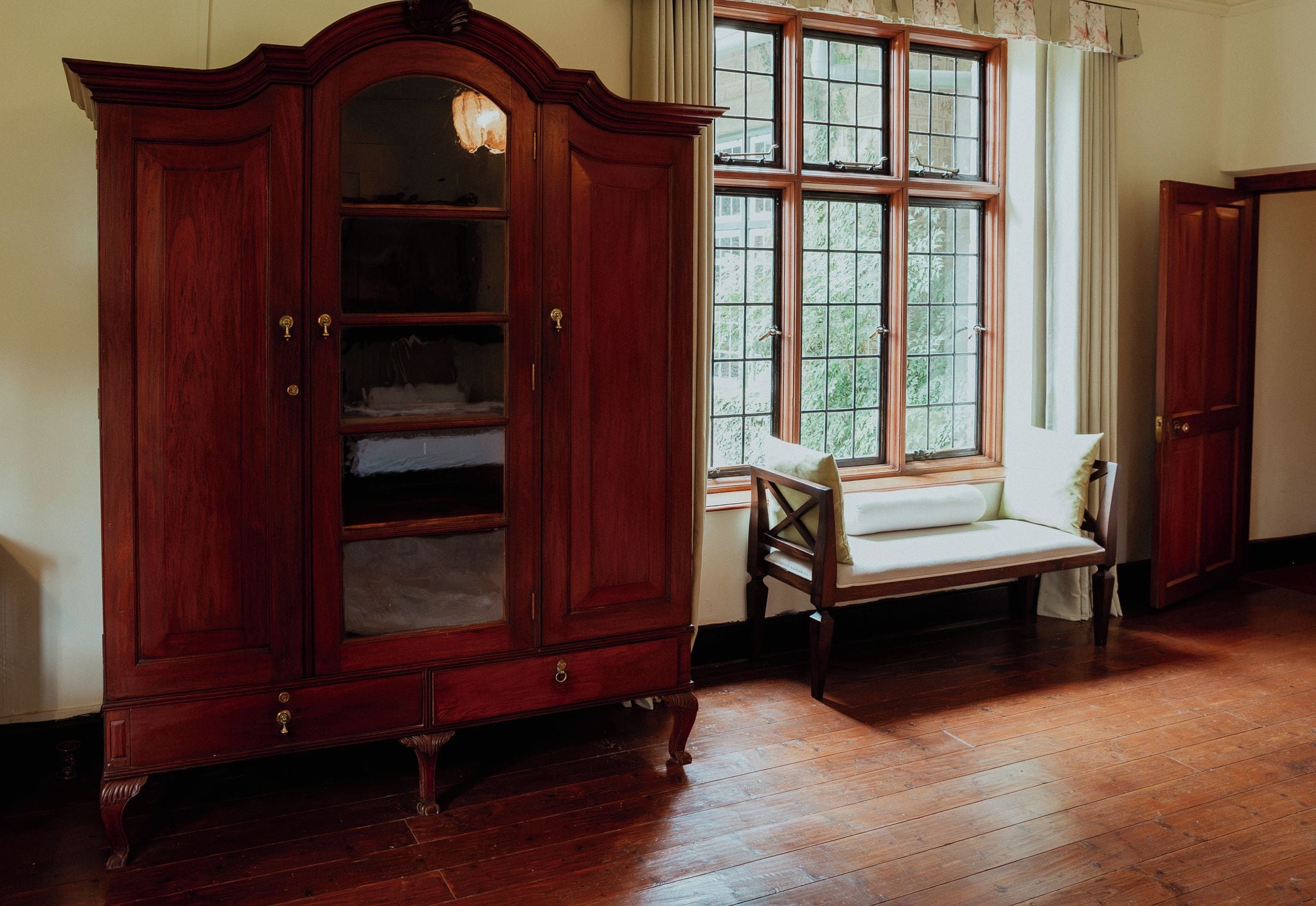Une pièce comprenant une grande armoire en bois, une fenêtre à carreaux et une chaise en bois.
